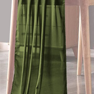 May include: A green table runner made of sheer fabric. The runner is draped over a wooden table and has a soft, flowing texture.