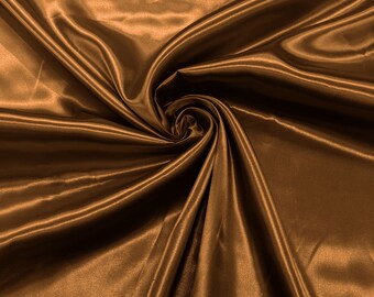 Op de afbeelding: Een close-up van een gladde, bruine satijnen stof met een zachte, vloeiende textuur. De stof is gedrapeerd en gevouwen, wat een luxe en elegante uitstraling creëert.