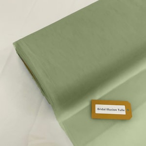 May include: A roll of sage green bridal illusion tulle fabric. The fabric is sheer and lightweight. The label reads "Bridal Illusion Tulle".