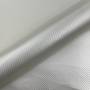 May include: A roll of white fabric with a woven, diagonal pattern. The material has a subtle sheen and appears tightly woven. The fabric is rolled, showing the texture and construction of the material.