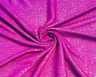 May include: A close-up of a pink fabric with sequins. The fabric is folded and has a soft, shimmery texture.