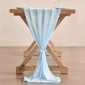 May include: A light blue table runner draped over a wooden table. The runner is tied in a bow at the center of the table.
