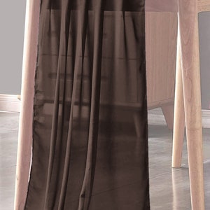 May include: A brown sheer table runner draped over a wooden table. The runner is made of a lightweight fabric and has a soft, flowing texture.