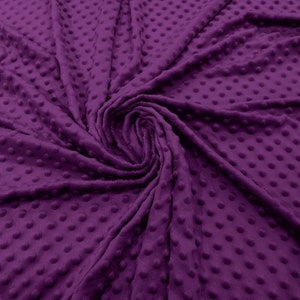 Puede incluir: Tela texturizada de color morado con un patrón de puntos. La tela es suave y afelpada, y es perfecta para hacer mantas, almohadas u otros artículos de decoración del hogar.