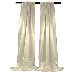 May include: Two ivory satin curtains hanging from a black rod. The curtains are long and flowy, with a soft, luxurious feel.
