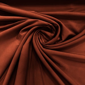 May include: Close-up of a rust-colored fabric with a soft, smooth texture. The fabric is draped and folded, creating a swirling pattern.