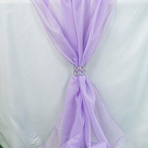 Pode incluir: Um corredor de mesa lavanda feito de tecido transparente com um anel prateado decorativo que segura o tecido no lugar.