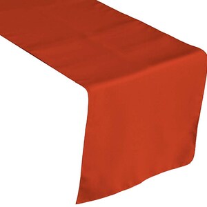 May include: A solid burnt orange table runner. The runner is made of a smooth, wrinkle-free fabric.