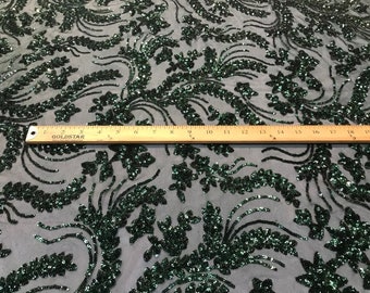 May include: Emerald green sequined fabric with a floral pattern. The fabric is shown with a ruler for scale.