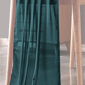 以下が含まれることがあります： 薄い生地のティールブルーのテーブルランナー。ランナーは木製のテーブルにかけられています。