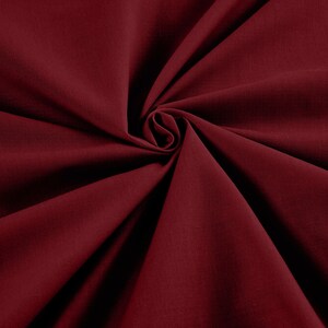May include: A close-up shot of a deep burgundy fabric, artfully arranged in a spiral. The material appears to be soft and flowing, with subtle texture and folds. The rich color and drape suggest a luxurious textile.
