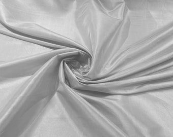 May include: A close-up of a smooth, white fabric with a soft, silky texture. The fabric is draped and folded, creating a flowing, elegant look.