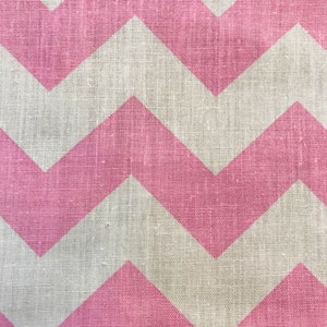 May include: Close-up of a fabric with a pink and white chevron pattern. The pink chevrons are wide and evenly spaced, creating a bold, graphic design. The fabric has a textured appearance, suggesting a natural fiber like linen or burlap.