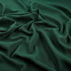 May include: A close-up of a deep green fabric with a smooth, slightly textured surface. The fabric is draped and folded, creating soft, flowing lines.