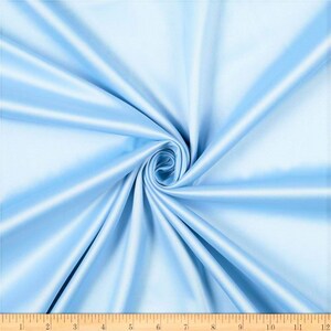 May include: A close-up of a light blue satin fabric. The fabric is smooth and silky, with a slight sheen. It is folded in a way that creates a swirl pattern.