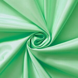 May include: A close-up of a smooth, light green fabric with a soft, flowing texture. The fabric is folded and draped to create a swirling pattern.