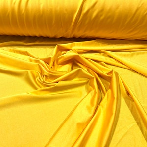 May include: A close-up of a bright yellow fabric with a smooth, silky texture. The fabric is draped and folded, showcasing its soft and flowing nature.