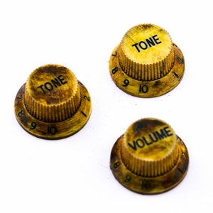 May include: Three vintage-style guitar knobs with a yellowed, aged appearance. The knobs are labeled "TONE" and "VOLUME" with numbers 1-10 around the edges.