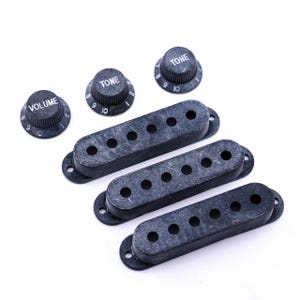 Könnte beinhalten: Drei schwarze Gitarren-Tonabnehmerabdeckungen und drei schwarze Knöpfe mit weißer Beschriftung. Die Knöpfe sind mit "Volume" und "Tone" beschriftet.