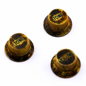 Könnte beinhalten: Drei Vintage-Gitarrenknöpfe mit schwarzem Text auf gelbem Hintergrund. Die Knöpfe sind mit "TONE" und "VOLUME" beschriftet und haben die Zahlen 6 bis 10 am Rand.