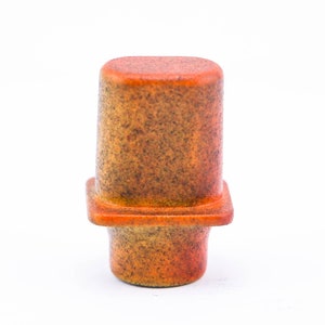 May include: A small, orange and brown ceramic vase with a square base and a rounded top.