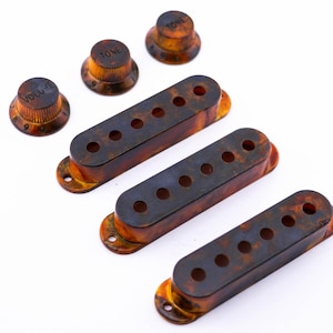 Può includere: Tre coperture per pickup di chitarra in tartaruga e tre manopole con le etichette "Volume" e "Tono".