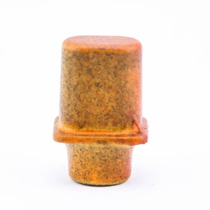 May include: A small, ceramic, orange and brown bottle stopper with a square base.
