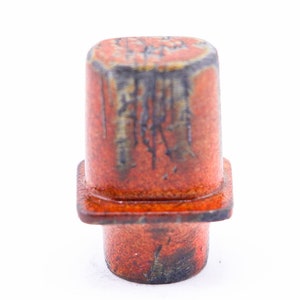 May include: A small, ceramic, orange and black, square-shaped bottle stopper.