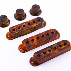 Könnte beinhalten: Drei Gitarren-Tonabnehmerabdeckungen aus Schildpatt und drei Knöpfe mit den Beschriftungen "Volume", "Tone" und "Tone".