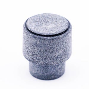 May include: A gray, round, textured knob with a black rim. The knob is made of a material that looks like stone.
