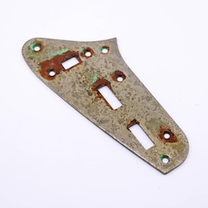 Op de afbeelding: Een zilverkleurige metalen gitaar pickguard met drie uitsparingen voor knoppen en een grote uitsparing voor een pickup. De pickguard heeft een versleten, verweerde uitstraling met roest en groene patina.