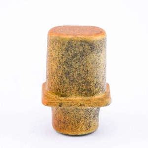 May include: A ceramic knob with a speckled brown and yellow glaze. The knob has a square base and a rounded top.
