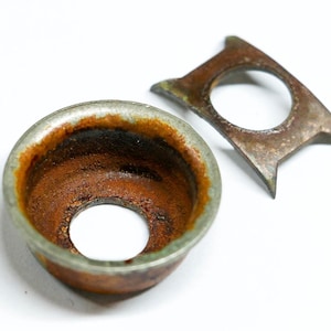 May include: Two antique metal objects with a weathered appearance. One is a circular, bowl-shaped piece with a central hole and a rusty brown interior. The other is a flat, geometric piece with a central hole and pointed edges.