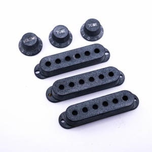 Könnte beinhalten: Drei schwarze Gitarren-Tonabnehmerabdeckungen und drei schwarze Knöpfe mit den Aufschriften "Volume", "Tone" und "Tone".