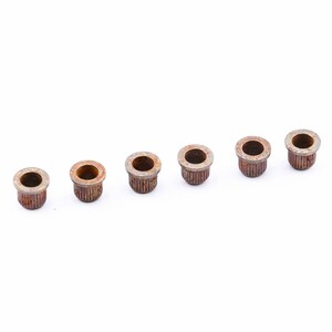 May include: Six rusty metal guitar string ferrules, arranged in a row on a white background.