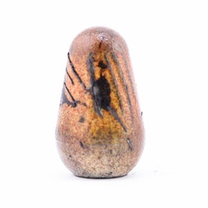 May include: A small, brown ceramic vase with a textured surface and black markings. The vase is shaped like a teardrop and has a rounded base.