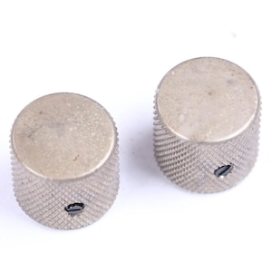 May include: Two silver-colored control knobs with a textured, ridged grip. The knobs have a flat top and a small, oval-shaped hole. The knobs are likely for an electronic device, such as a guitar amplifier or stereo.