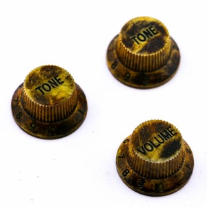 Könnte beinhalten: Drei vintage goldfarbene Gitarrenknöpfe mit schwarzer Beschriftung. Die Knöpfe sind mit "TONE" und "VOLUME" beschriftet und haben die Zahlen 6-10 am Rand.
