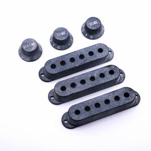 Könnte beinhalten: Drei schwarze Gitarren-Tonabnehmerabdeckungen und drei schwarze Knöpfe mit weißer Beschriftung. Die Knöpfe sind mit "Volume", "Tone" und "Tone" beschriftet.