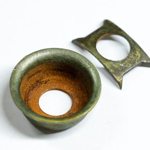 May include: Two antique metal objects. One is a round, bowl-shaped piece with a green and brown patina. The other is a square-shaped piece with a hole in the center and pointed edges, also with a green and brown patina.