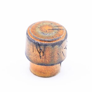 May include: A ceramic knob with a brown and orange glaze. The knob has a circular top and a cylindrical base. The top of the knob has a dark brown rim and a light brown center with a pattern of black lines.