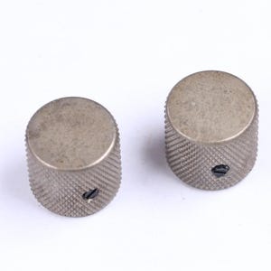 May include: Two silver-toned guitar knobs with a knurled grip and a flat top. The knobs have a small screw hole and are set against a white background. These are replacement parts for musical instruments.