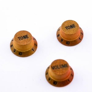 Könnte beinhalten: Drei Gitarrenknöpfe mit brauner und goldener Oberfläche. Die Knöpfe sind mit "TONE" und "VOLUME" sowie den Zahlen 1 bis 10 beschriftet.