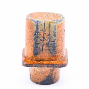 May include: A small, orange and black ceramic vase with a square base and a cylindrical top. The vase has a textured surface and a unique, abstract design.