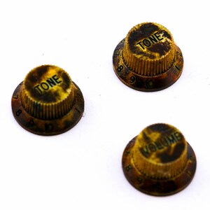 Könnte beinhalten: Drei Vintage-Gitarrenknöpfe mit Schildpattmuster. Die Knöpfe sind mit "TONE" und "VOLUME" sowie den Zahlen 0-10 beschriftet.