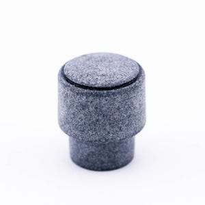 May include: A gray stone knob with a smooth, textured surface. The knob has a black ring around the top.