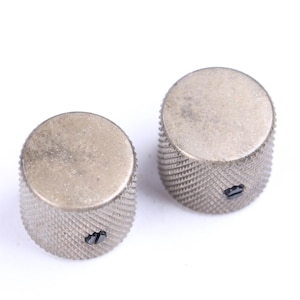May include: Two silver-toned control knobs with a textured, ridged design on the sides and a flat top. Each knob has a small, dark screw. The knobs are likely for an electronic device, such as a guitar or amplifier.