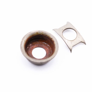 May include: Two metal parts, one a small cup-shaped piece with a rusty interior and a hole in the center, the other a flat, curved piece with a hole in the center.