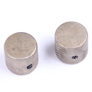 May include: Two silver-toned metal knobs with a ridged, cylindrical body and a flat, circular top. Each knob has a small, dark screw visible on the side. The knobs are likely for a musical instrument or electronic device.