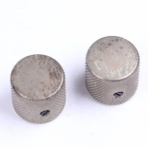 以下が含まれることがあります： 銀色の円筒形のノブが2つ。表面はテクスチャ加工され、溝があります。各ノブには小さな穴があり、摩耗の兆候が見られます。これらのノブは、楽器や電子機器用である可能性があります。